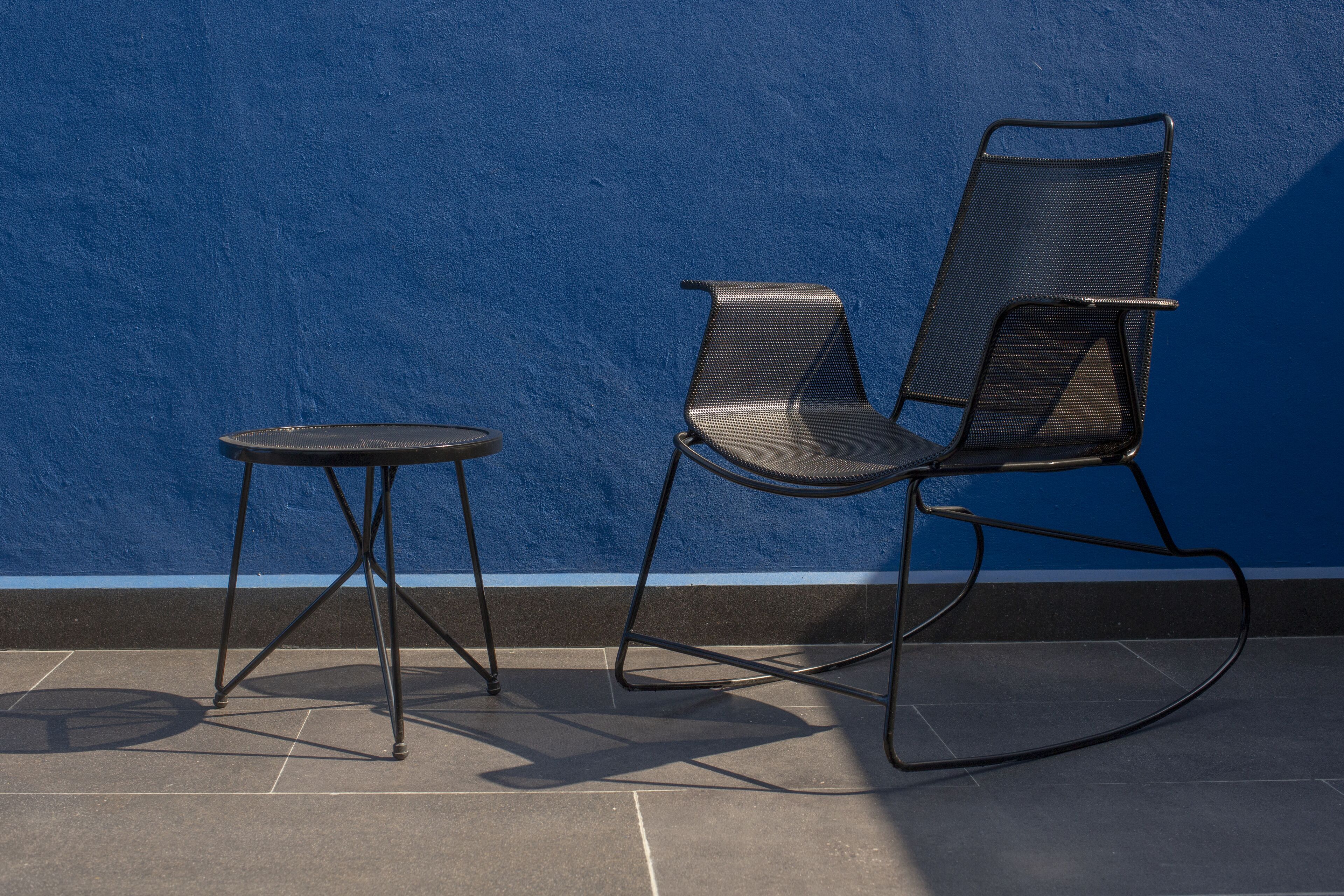 Un juego de silla y mesa de metal negro frente a una pared azul.