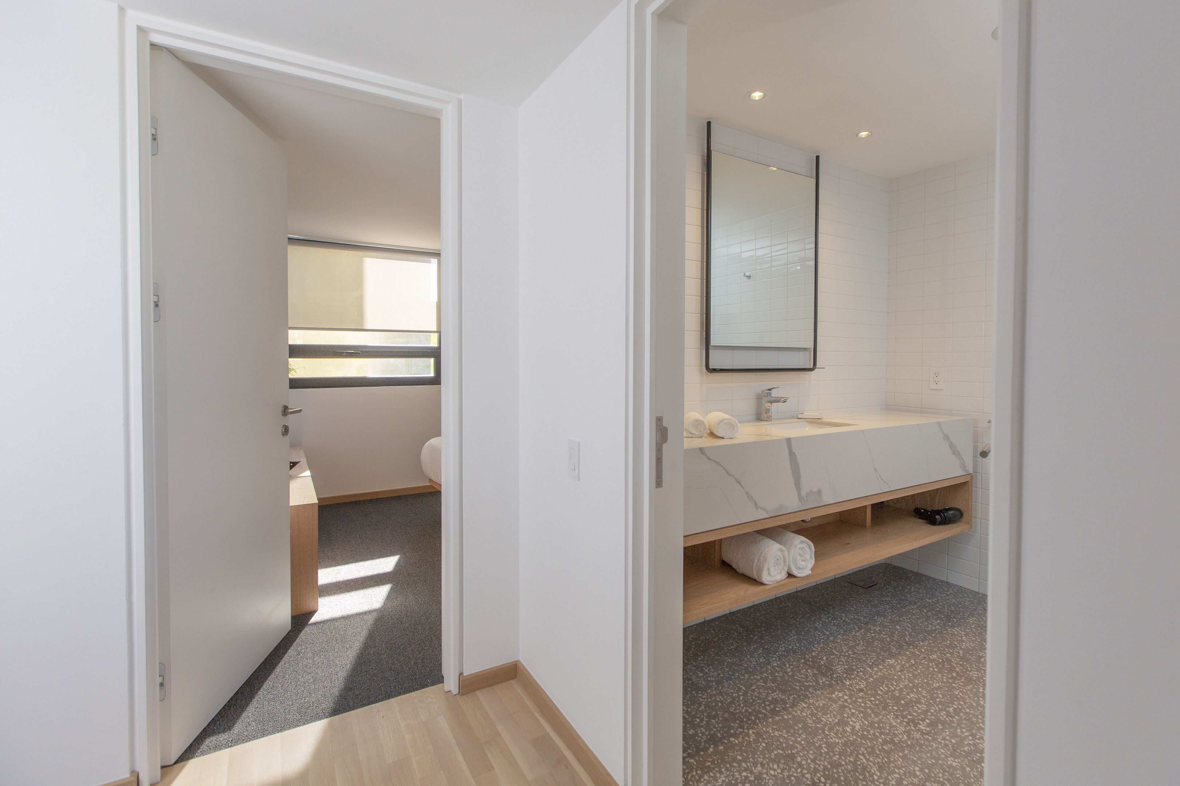 Une salle de bain moderne avec un meuble-lavabo blanc, un miroir et un espace douche visible à travers une porte ouverte.