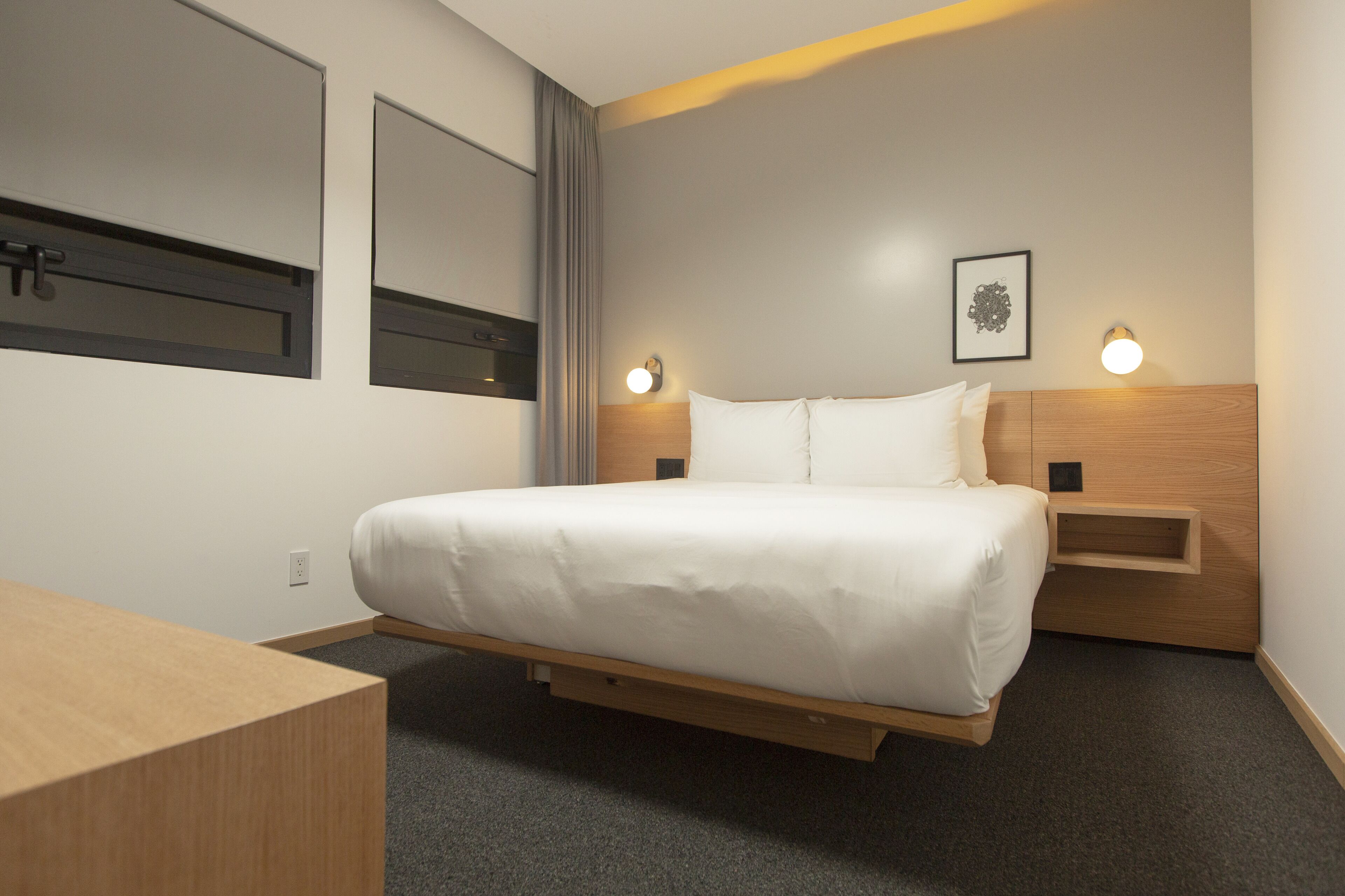 Quarto de hotel moderno com cama, mesas de cabeceira, escrivaninha e janela com cortinas.