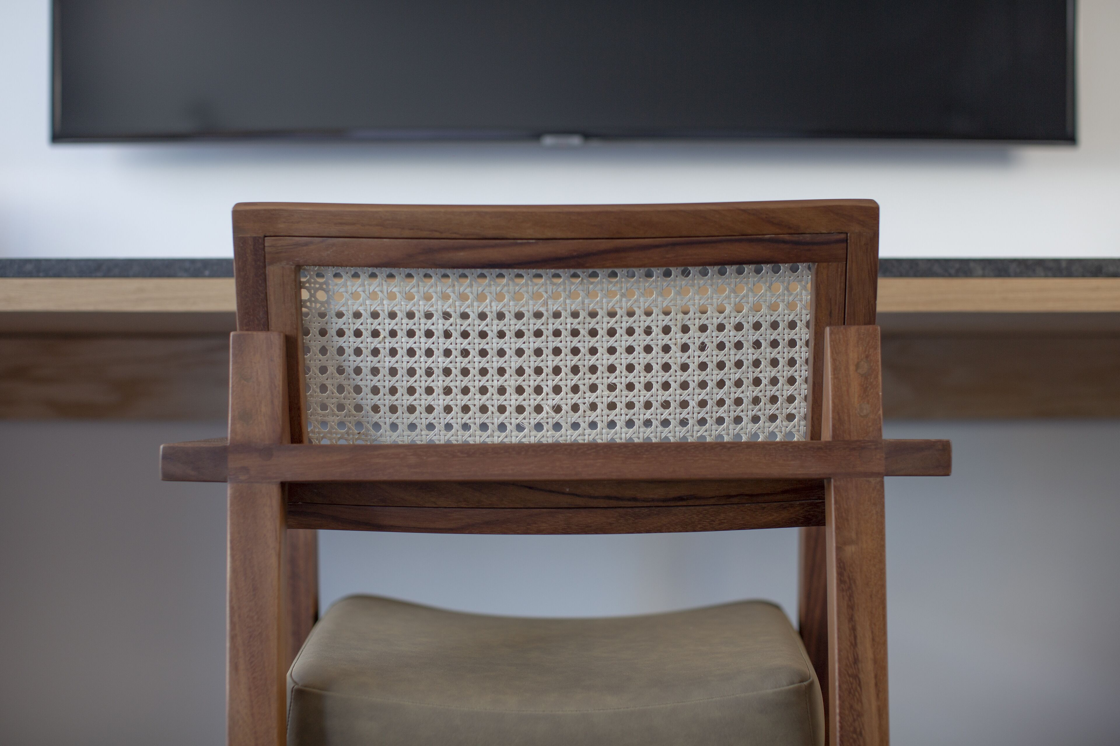 A wooden chair with a woven backrest and cushioned seat, positioned in front of a flat-screen TV mounted on a wall.