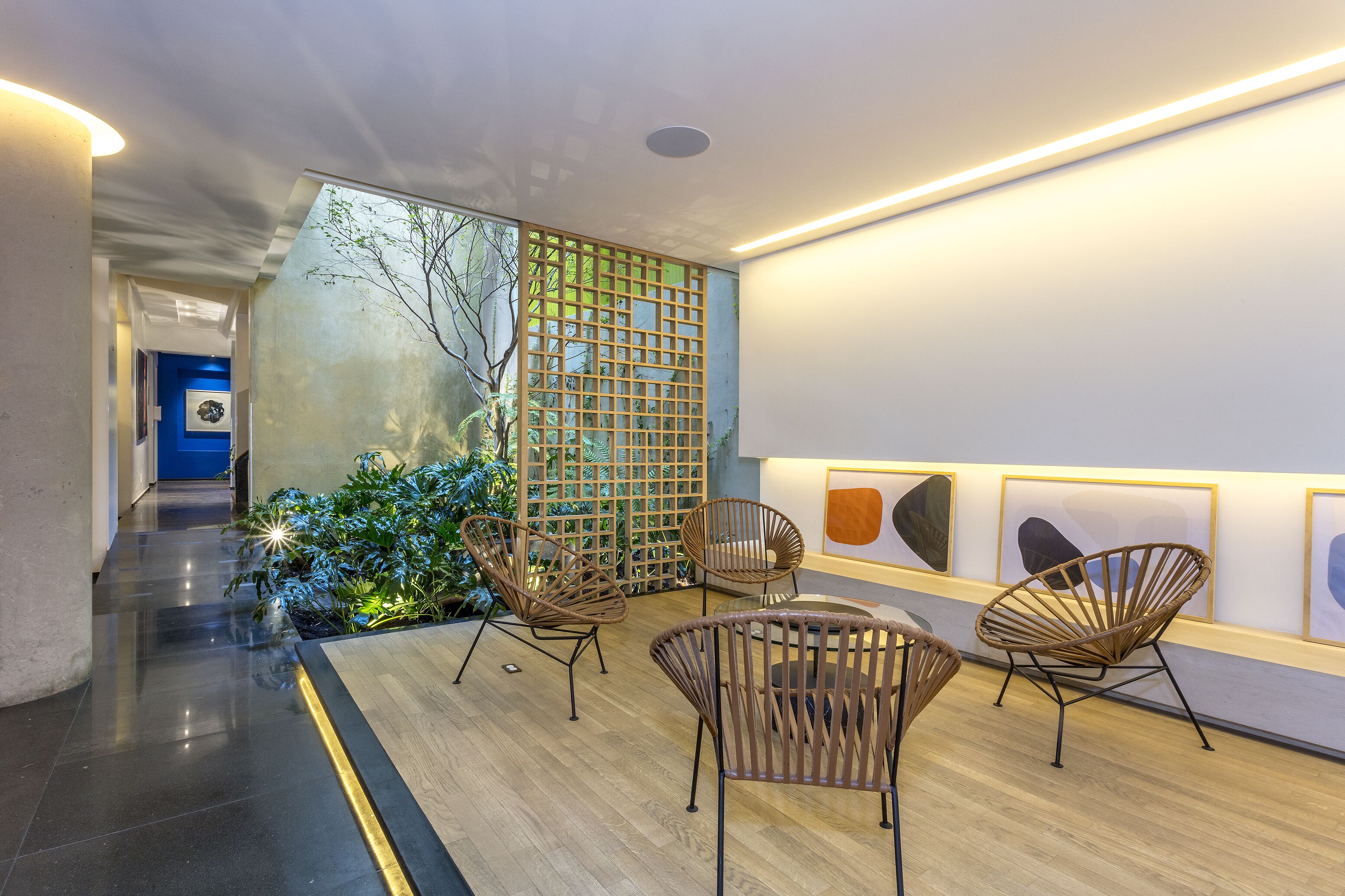 Ein modernes Interieur mit Holzboden, einer Sitzecke mit Korbstühlen, einer Wand mit abstrakter Kunst und Blick auf einen blauen Raum im Hintergrund.
