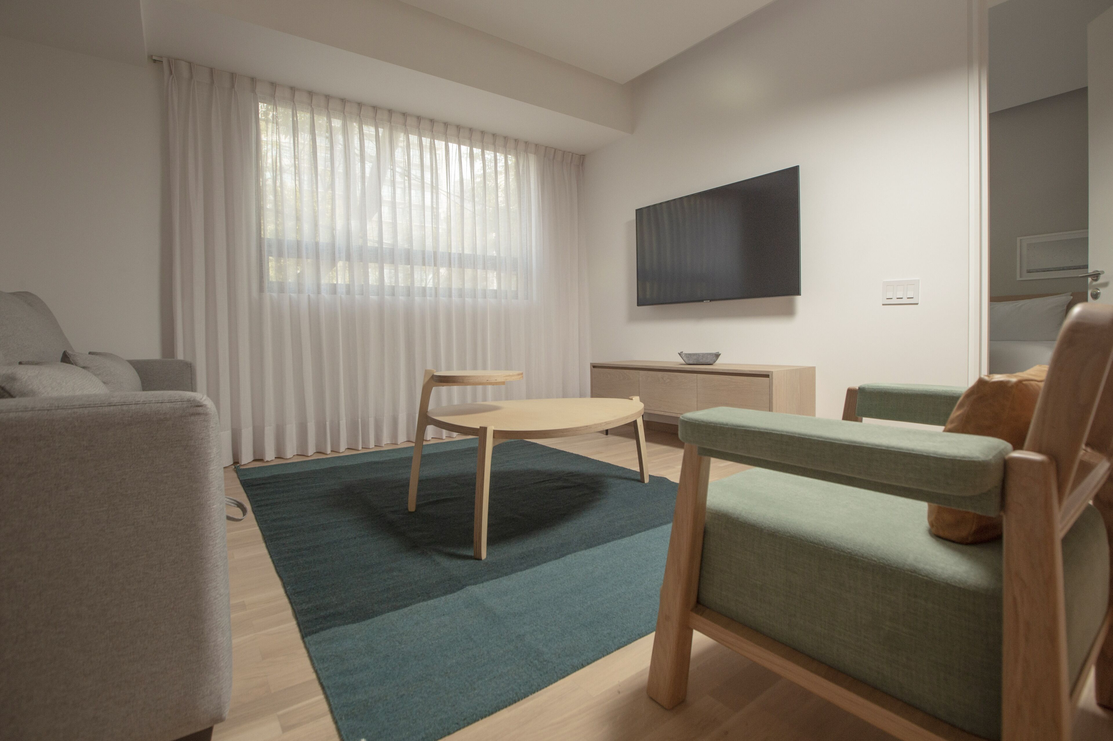 A modern living room with a sofa, a green armchair, a round wooden table, and a TV mounted on the wall.