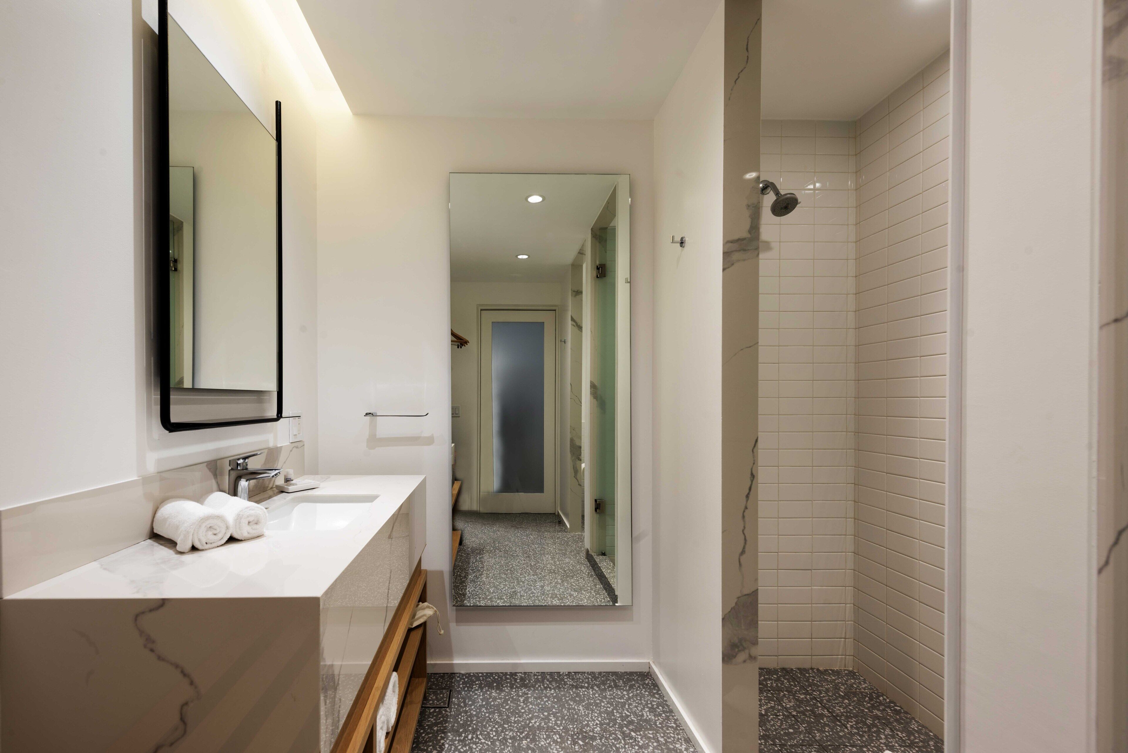 A modern bathroom with a marble vanity, a large mirror, and a shower area.