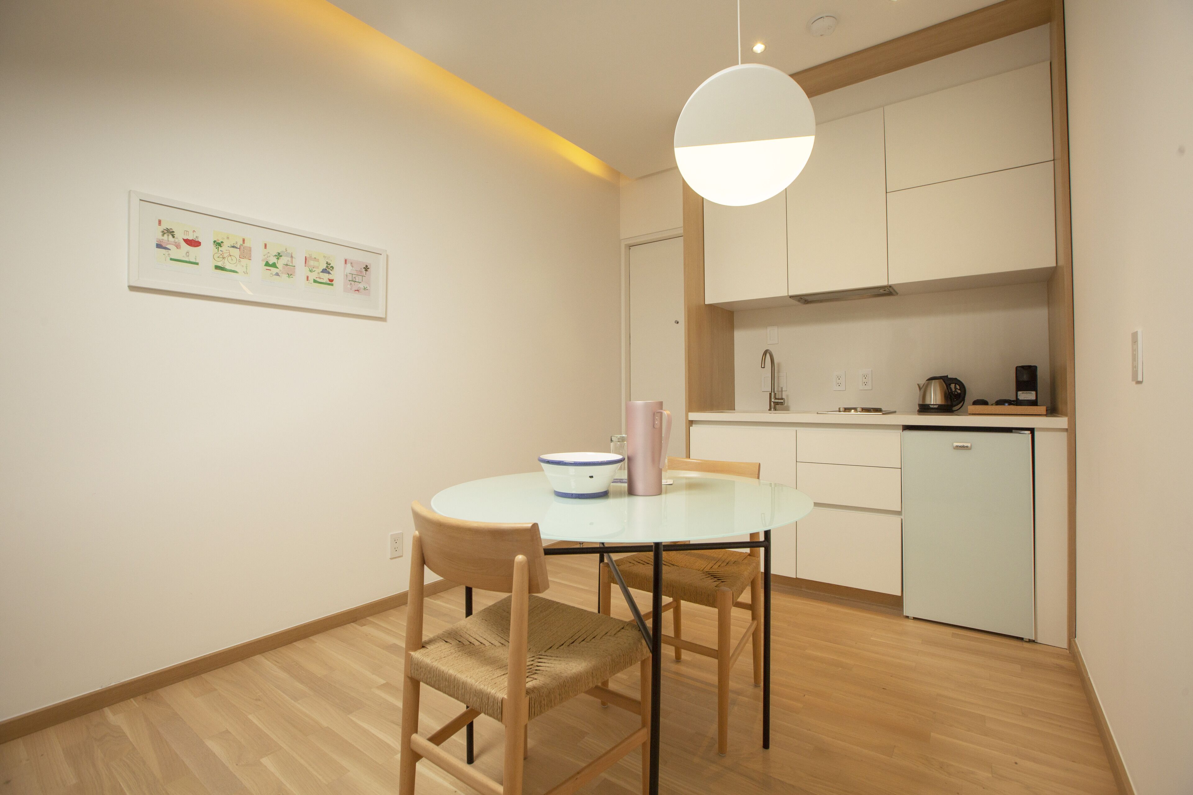 Una cocina moderna con armarios blancos, un refrigerador pequeño y una cafetera.