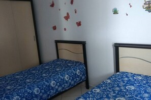A room with two single beds with floral-patterned bedding, a wooden wardrobe, and a wall decorated with red flower stickers and a few small toys. - COMFORTABLE APARTMENT WITH SEA VIEWS (Praia Grande)