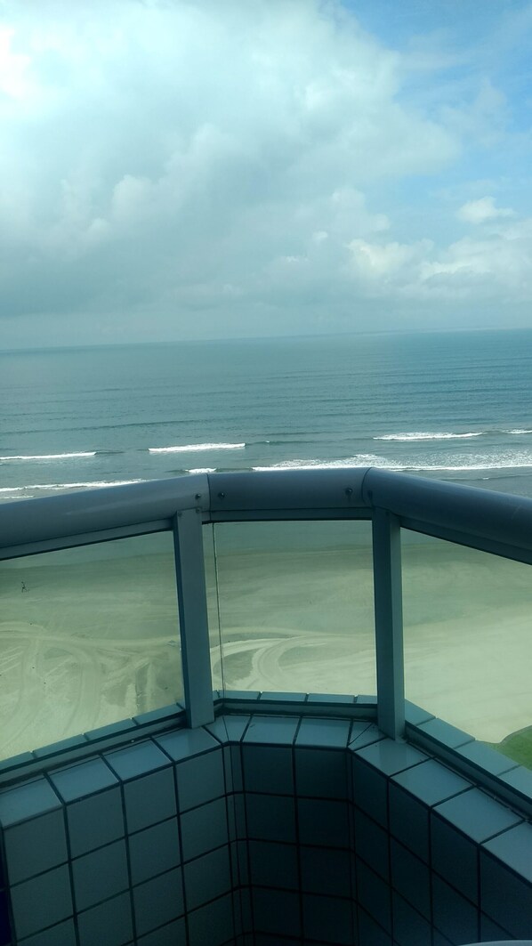 A view from a balcony overlooking a beach with waves, a cloudy sky, and a distant horizon. - COMFORTABLE APARTMENT WITH SEA VIEWS (Praia Grande)