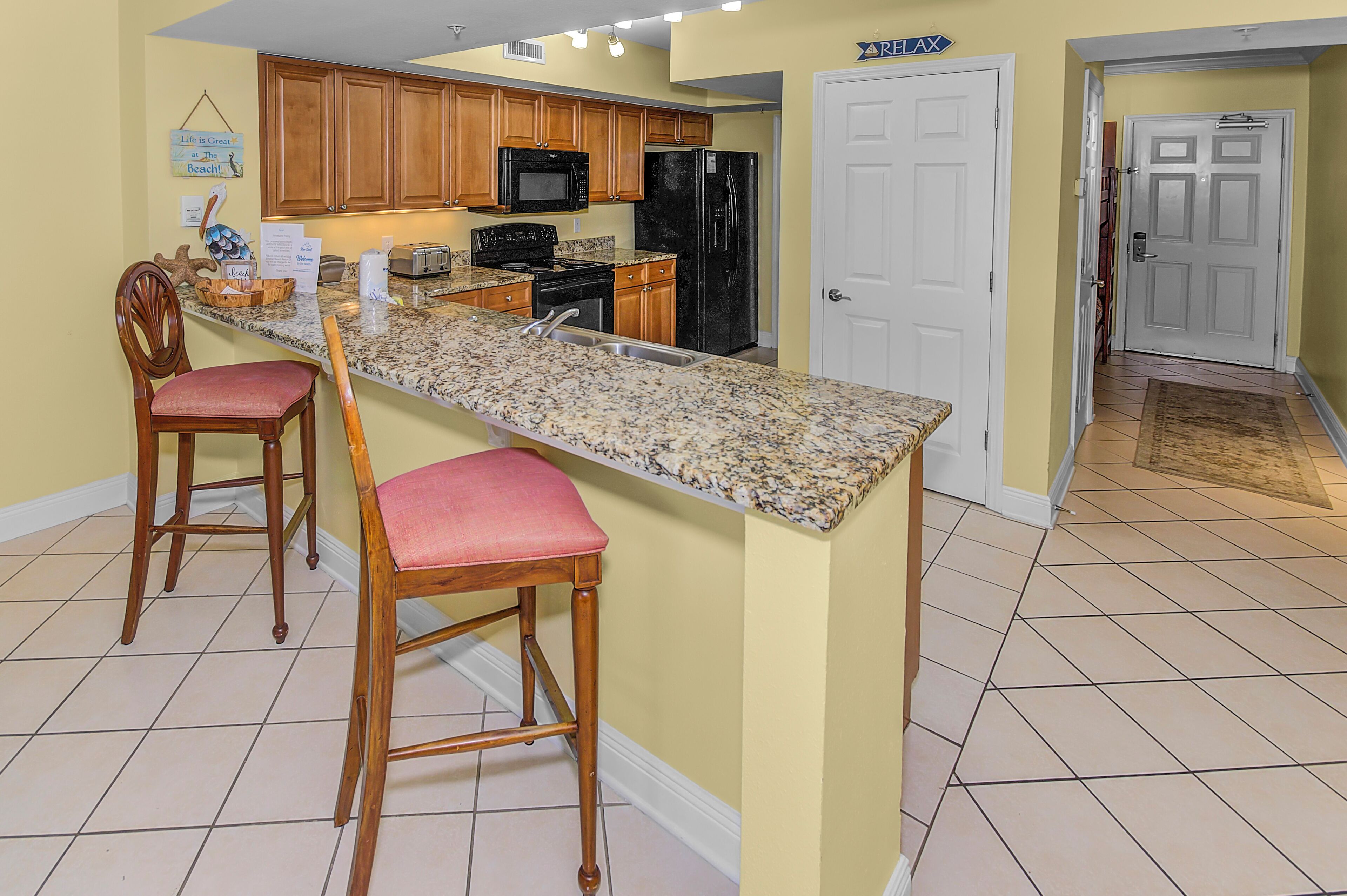 A kitchen with wooden cabinets, a granite countertop, a refrigerator, and two bar stools.