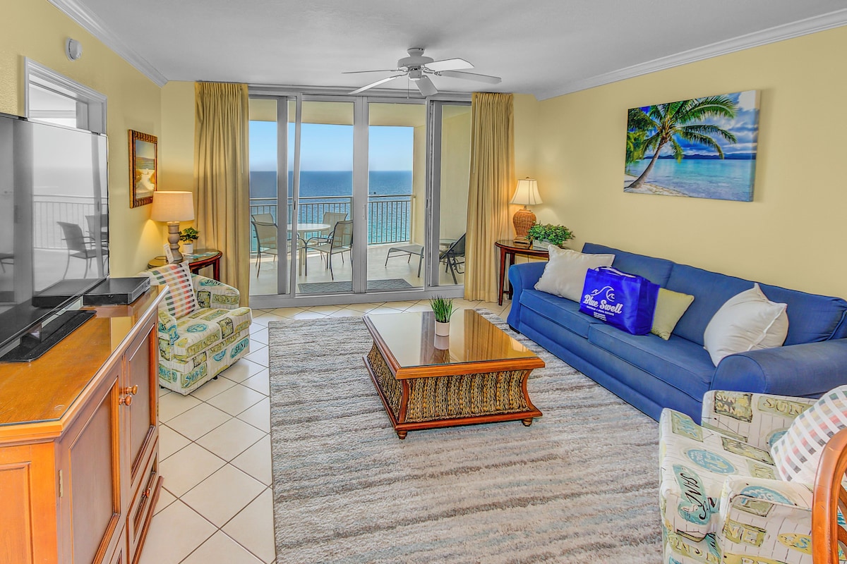 A living room with a blue sofa, a wooden coffee table, and a view of the ocean through a sliding glass door.