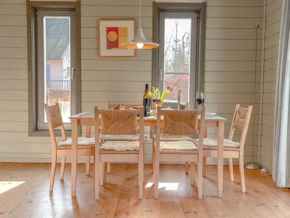 Un comedor con una mesa y sillas de madera, una lámpara colgante y una obra de arte enmarcada en la pared.