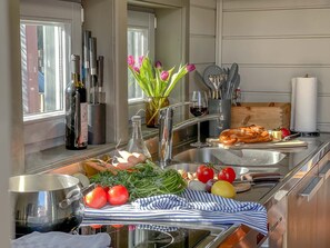 Una cocina moderna con un lavamanos de acero inoxidable, una botella de vino, verduras frescas y una tabla de cortar con un pretzel.