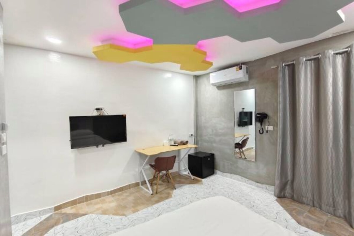 A modern hotel room with a bed, a desk, a chair, a flat-screen TV, a mirror, and a window with curtains.