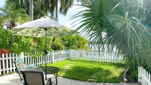 Un patio con una mesa, sillas, una valla blanca de piquetes y una palmera.
