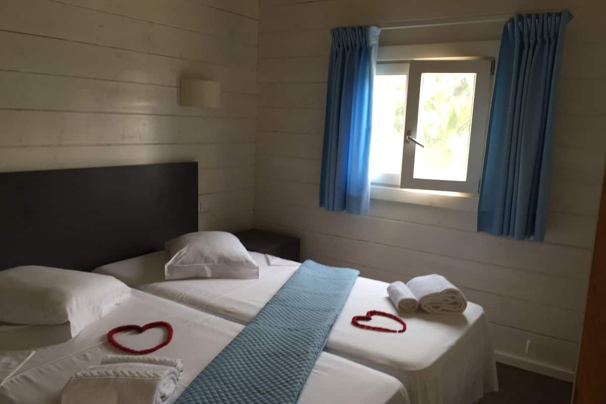 A room with two beds, a window with curtains, and towels on the beds.