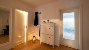 Una habitación con piso de madera, un armario blanco con cajones, un espejo y una puerta de vidrio esmerilado.