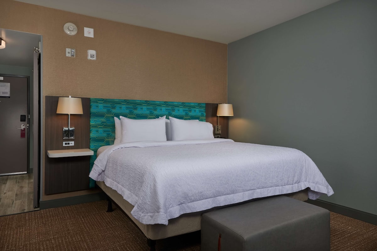 A hotel room with a bed, two bedside tables, a bench, and a door.