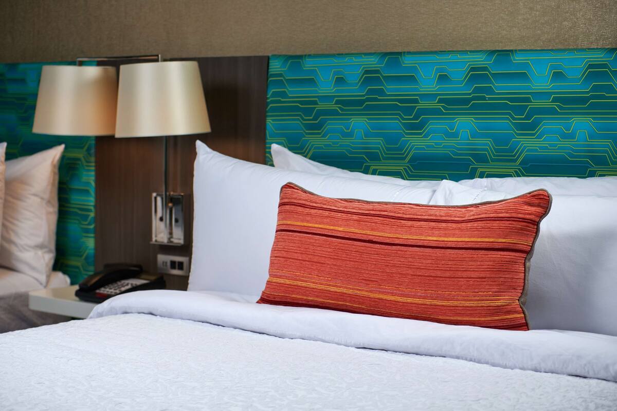 A hotel room with a bed, white bedding, a teal patterned headboard, and a lamp.