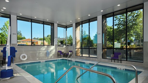 An indoor swimming pool with clear views of the outside, a lifeguard chair, and a no lifeguard sign. - Hampton Inn Sherwood Portland (Sherwood)
