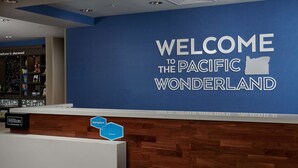 A reception desk with a blue wall displaying "WELCOME TO THE PACIFIC WONDERLAND" and a "Hilton Honors" sign. - Hampton Inn Sherwood Portland (Sherwood)