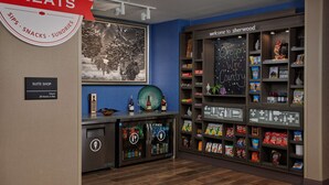 A suite shop with a 24-hour service sign, a beverage cooler, and a shelf stocked with snacks and sundries. - Hampton Inn Sherwood Portland (Sherwood)