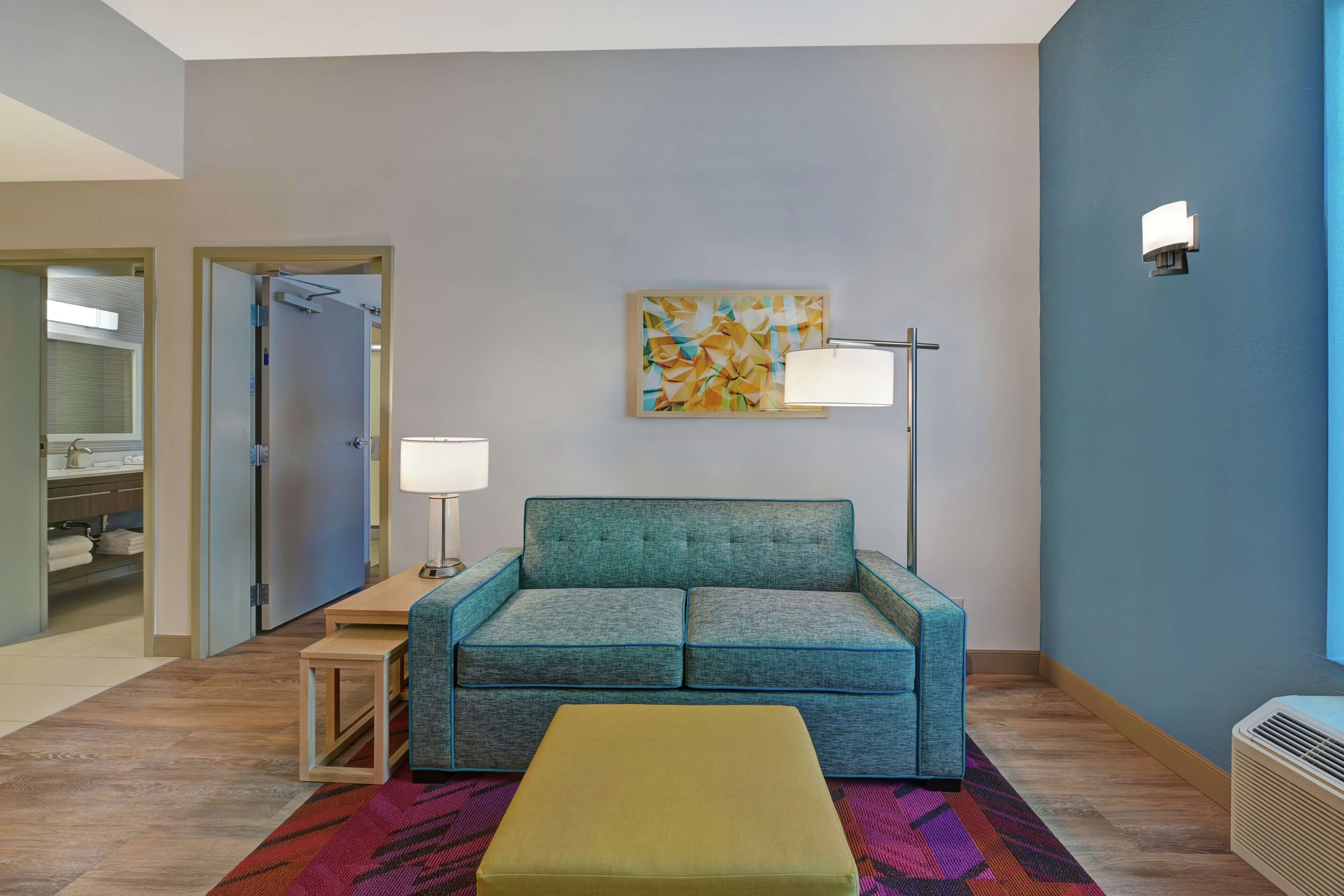 A modern living room with a teal sofa, a small wooden table, and a colorful rug.