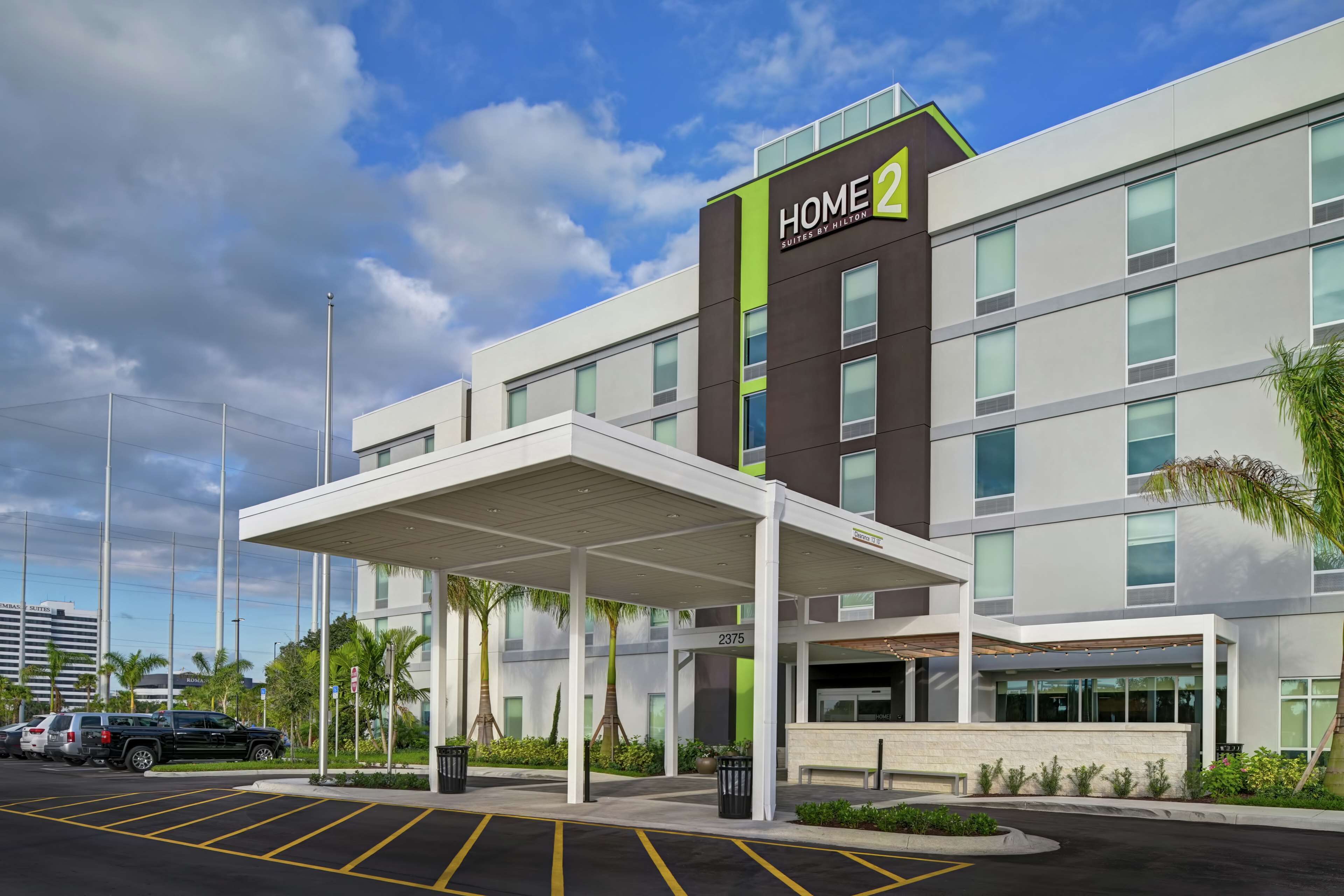A modern hotel with a covered entrance, a parking lot, and a clear sky.