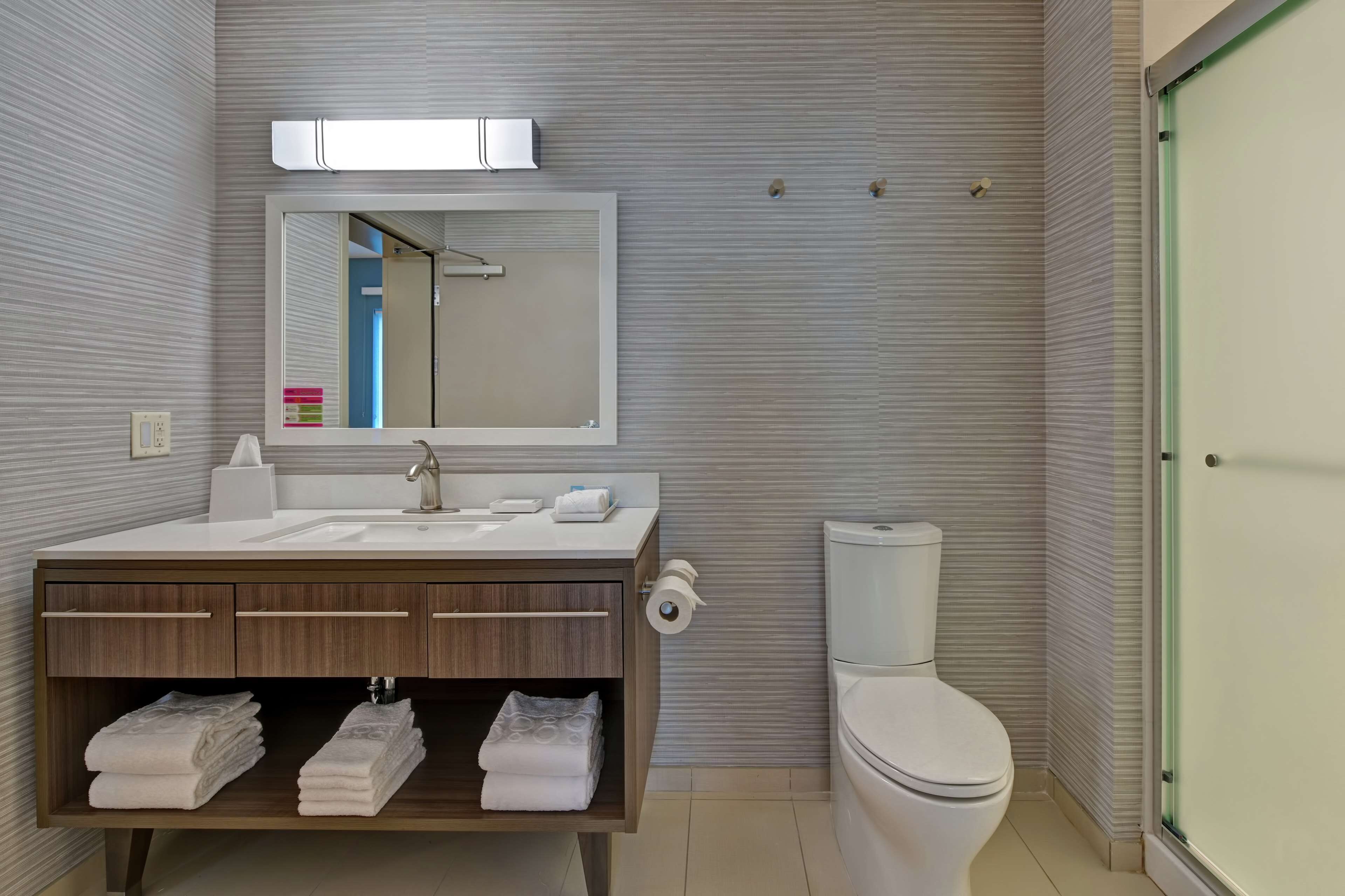 Une salle de bain moderne avec un grand miroir, un lavabo, des toilettes et un meuble-lavabo avec des serviettes.