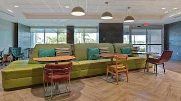A modern lounge area with a green sofa, red chairs, and a wooden table.