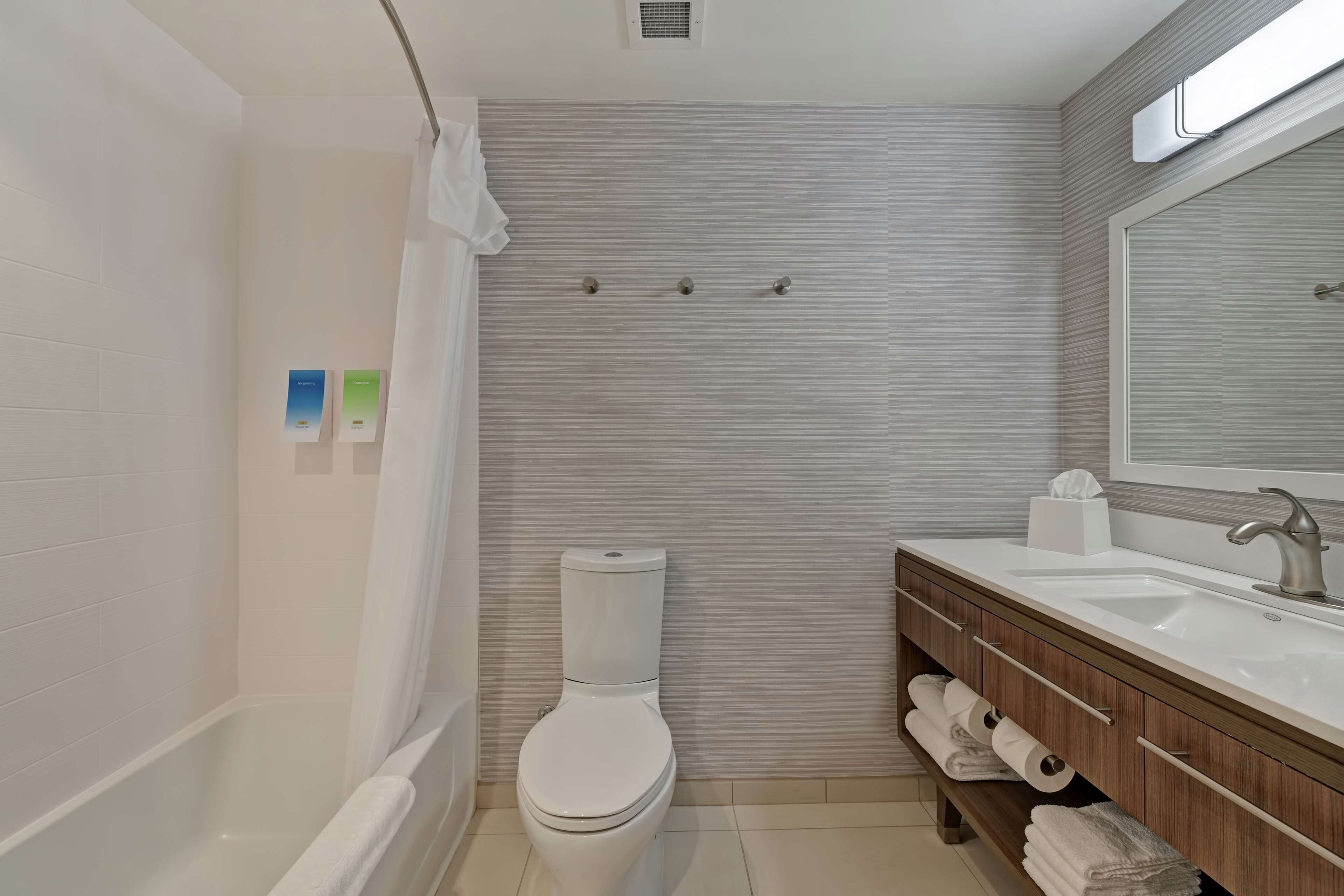 A modern bathroom with a white toilet, a bathtub, a vanity with a mirror, and a towel rack.