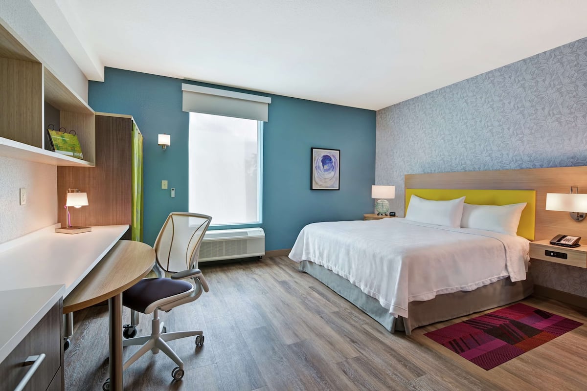 Et hotelværelse med skrivebord, stol, seng og et vindue.
