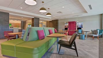 A modern lounge area with a green sofa, multiple tables, and chairs.