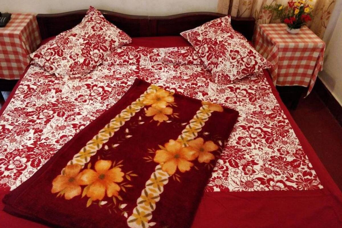 Ein Bett mit einer rot-weißen blumigen Tagesdecke, zwei passende Kissen und einer dekorativen orangefarbenen Blumenkomposition auf dem Bett.