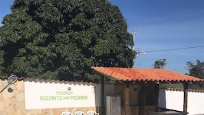 Un área de piscina con un muro de piedra, sillas de plástico blanco y un letrero que dice "POUSADA RECANTO DAS PEDRAS".