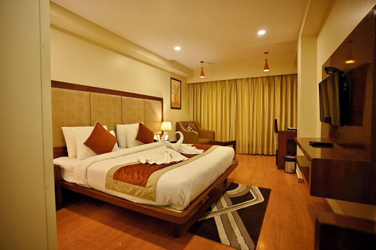 A hotel room with a large bed, a desk, a TV, and a chair.