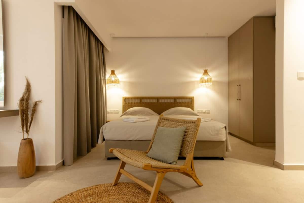 A bedroom with a bed, a wicker chair, a bedside table, and a window with curtains.