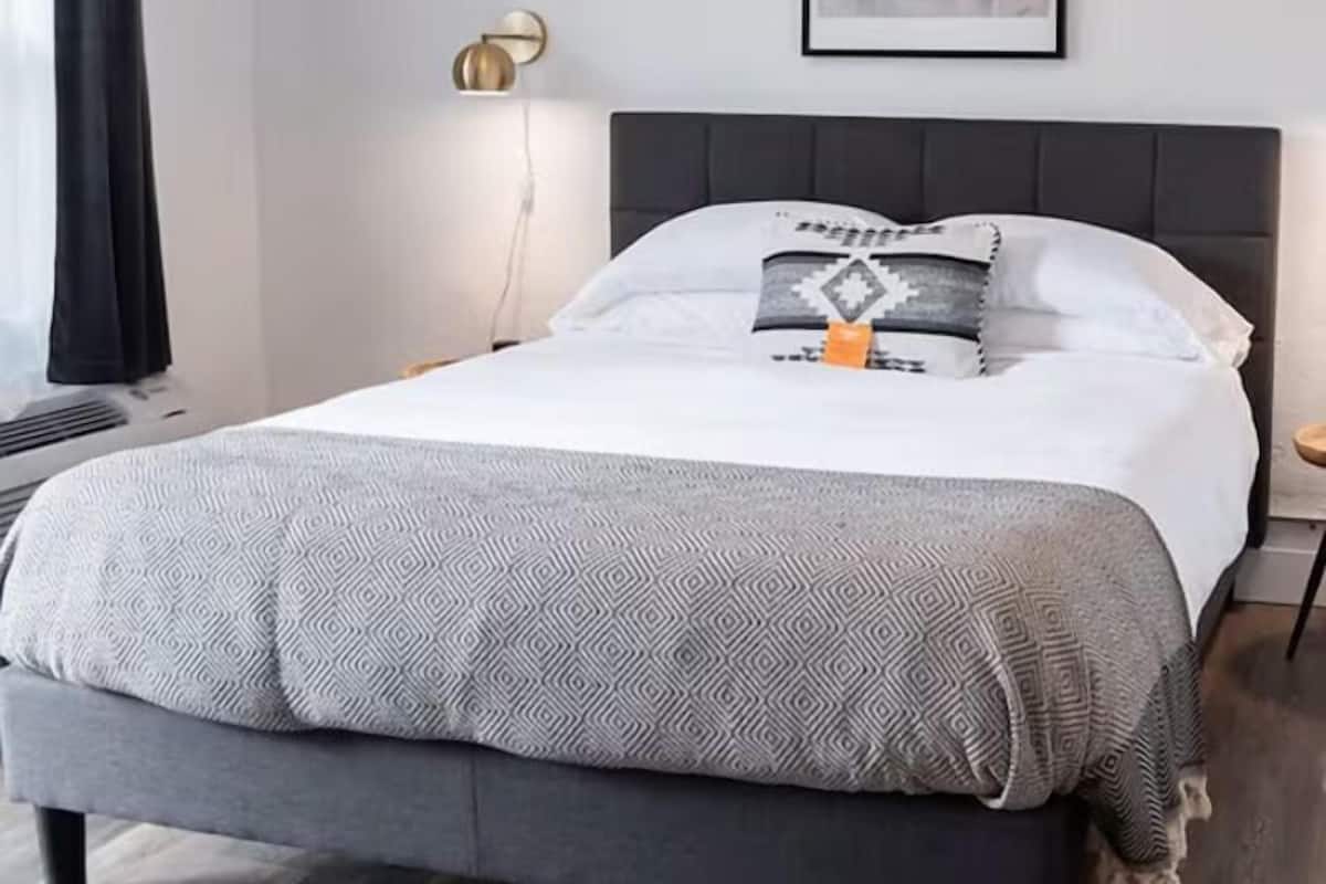 A neatly made bed with a patterned blanket, a headboard, and a wall-mounted light fixture.