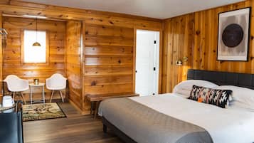 A wooden-paneled room with a bed, two white chairs, a small table, and a door.