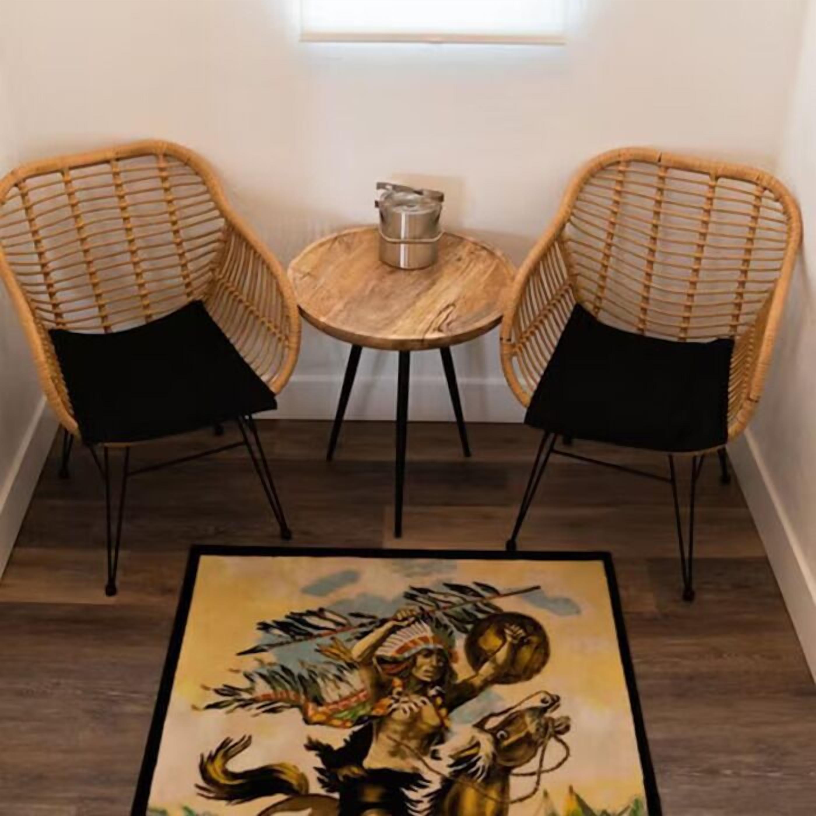 A room with two wicker chairs, a small round wooden table with a metal container, and a framed painting on the floor.