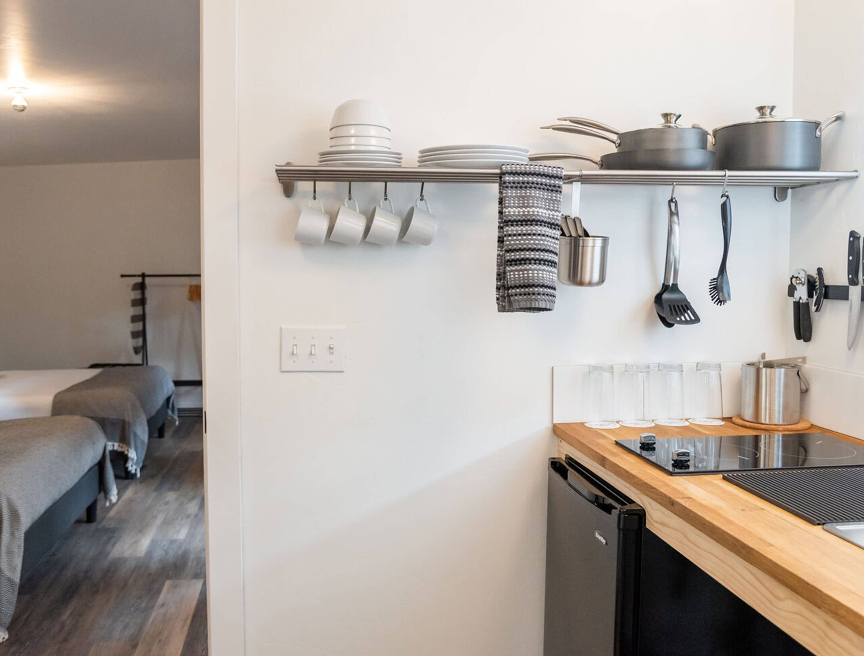 Una cocina compacta con encimera de madera, lavavajillas y estante empotrado con vajilla y utensilios.