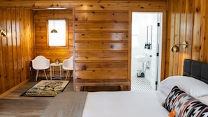 A wooden room with a bed, a desk, two chairs, a rug, and a bathroom visible through an open door. - The Nightingale Motel (Pagosa Springs)
