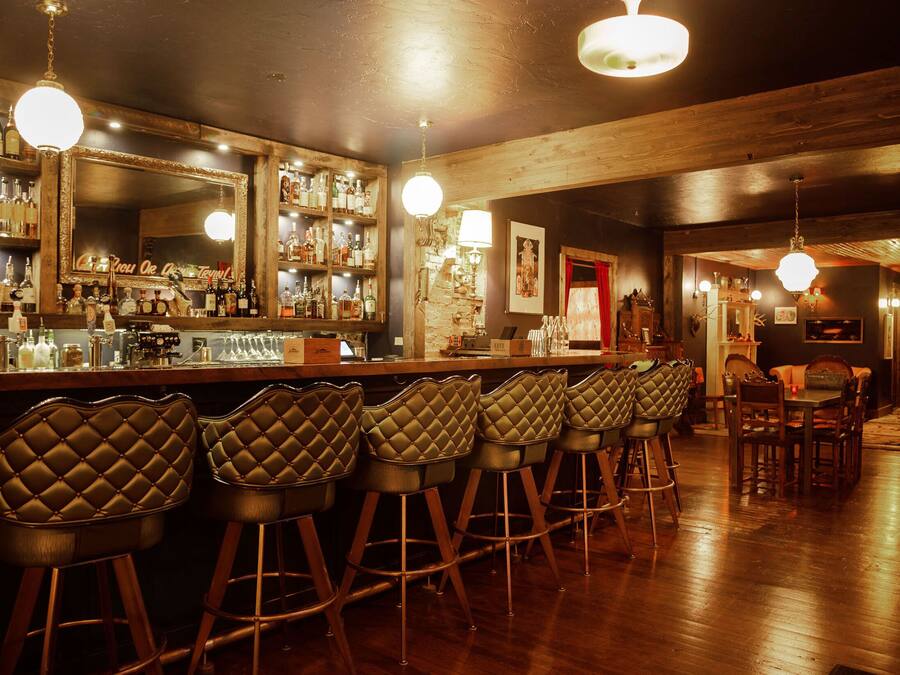 A bar area with multiple stools, a bar counter, and a mirror.