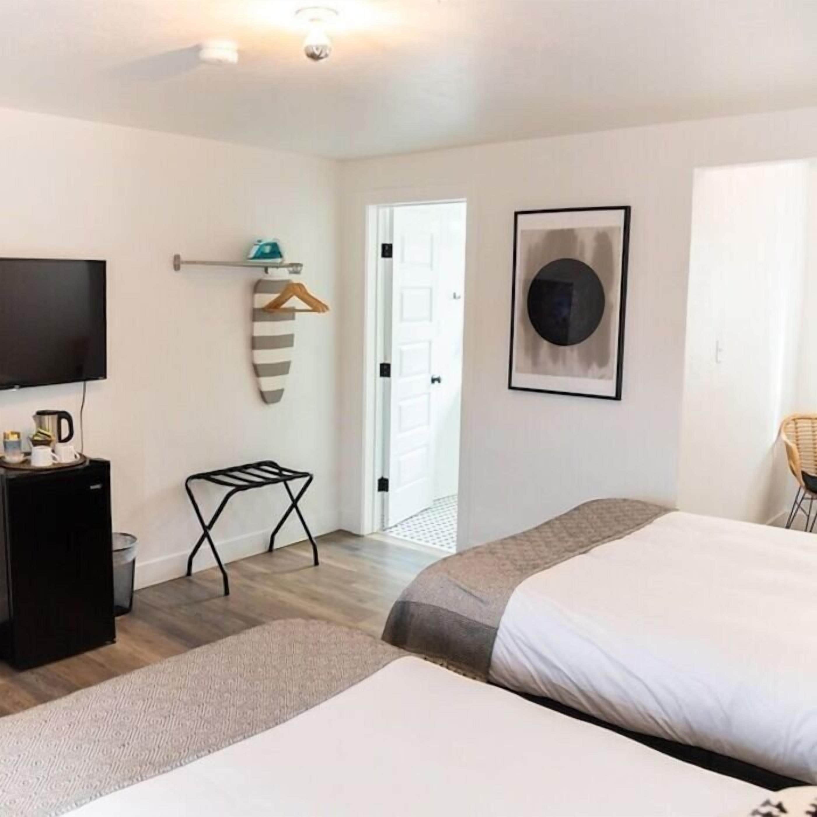 Une chambre d’hôtel équipée d’un lit, d’une télévision, d’une machine à café, d’un porte-manteau et d’un tableau encadré au mur.