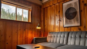 A cozy room with a wooden paneled wall, a grey sofa, a small table with a remote control, and a framed artwork. - The Nightingale Motel (Pagosa Springs)
