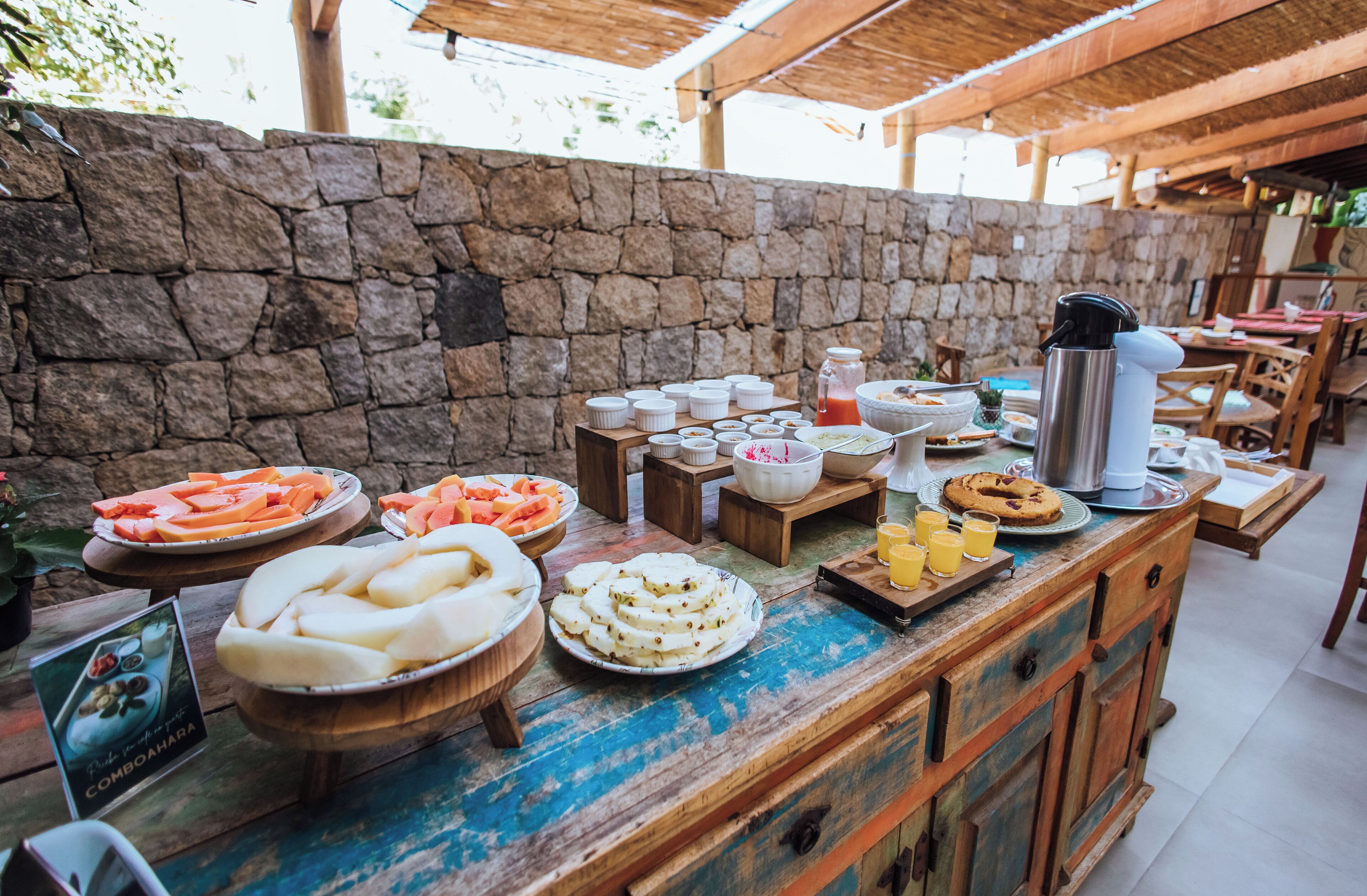A buffet setup with various food items and beverages on a wooden table under a stone wall.