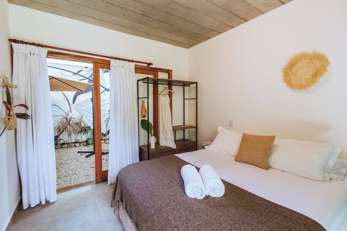 Un dormitorio con cama, una silla colgante y vistas del jardín a través de un ventanal.