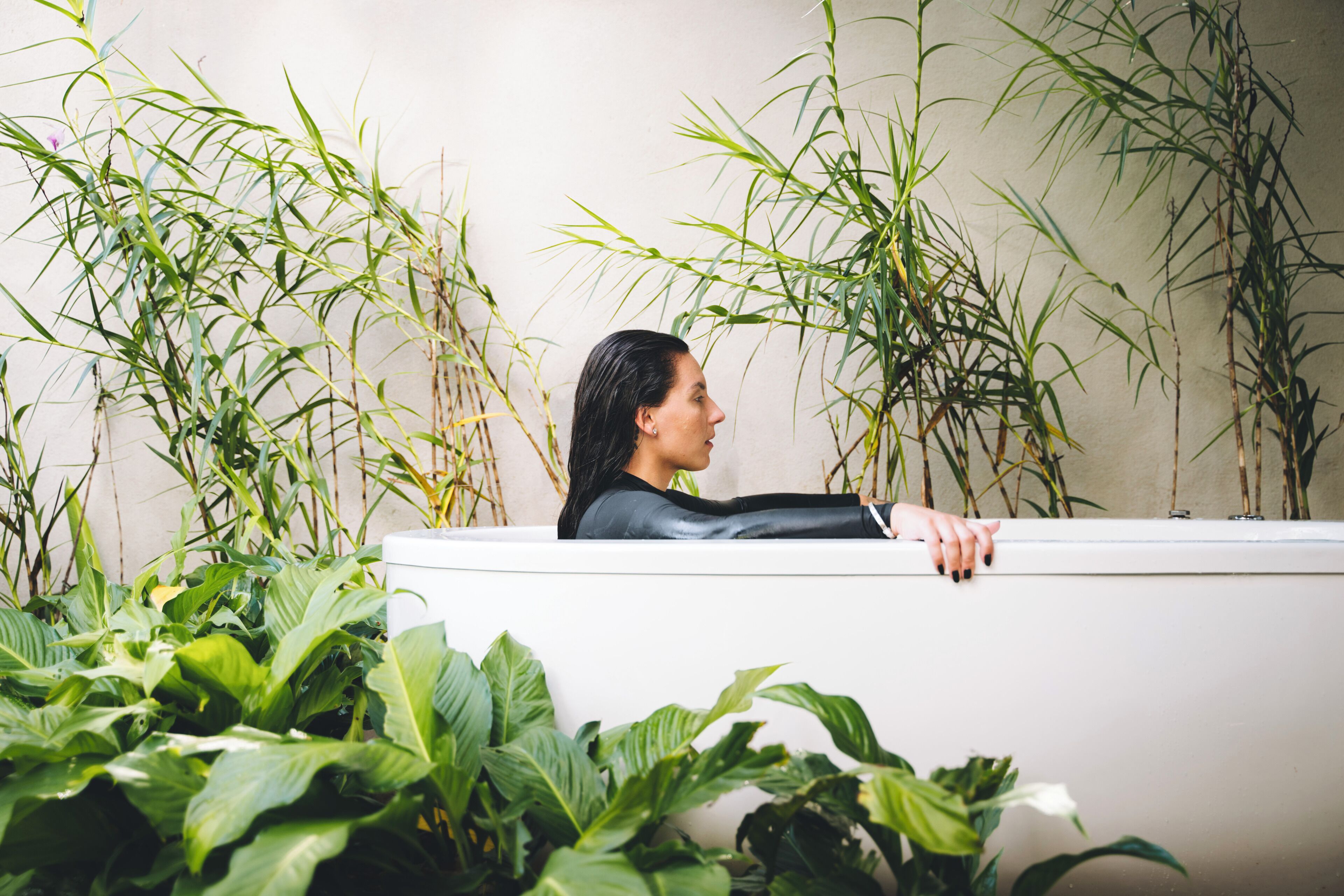 A person in a bathtub surrounded by lush green plants.