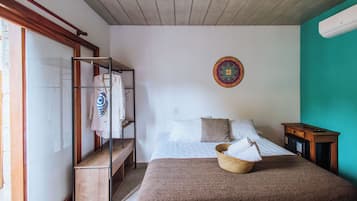 Ein Schlafzimmer mit einem Bett, einem Holzregal mit Kleidung, einem farbenfrohen Wandbehang und einer türkisblauen Akzentwand.
