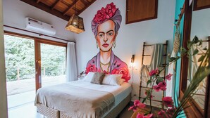 Une chambre avec un grand lit, une fresque murale, un luminaire suspendu et une fenêtre donnant sur un paysage verdoyant.