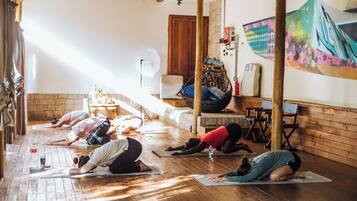 Ein Yoga-Kurs in einem Raum mit Holzboden, einer Steinwand und einem Wandgemälde.