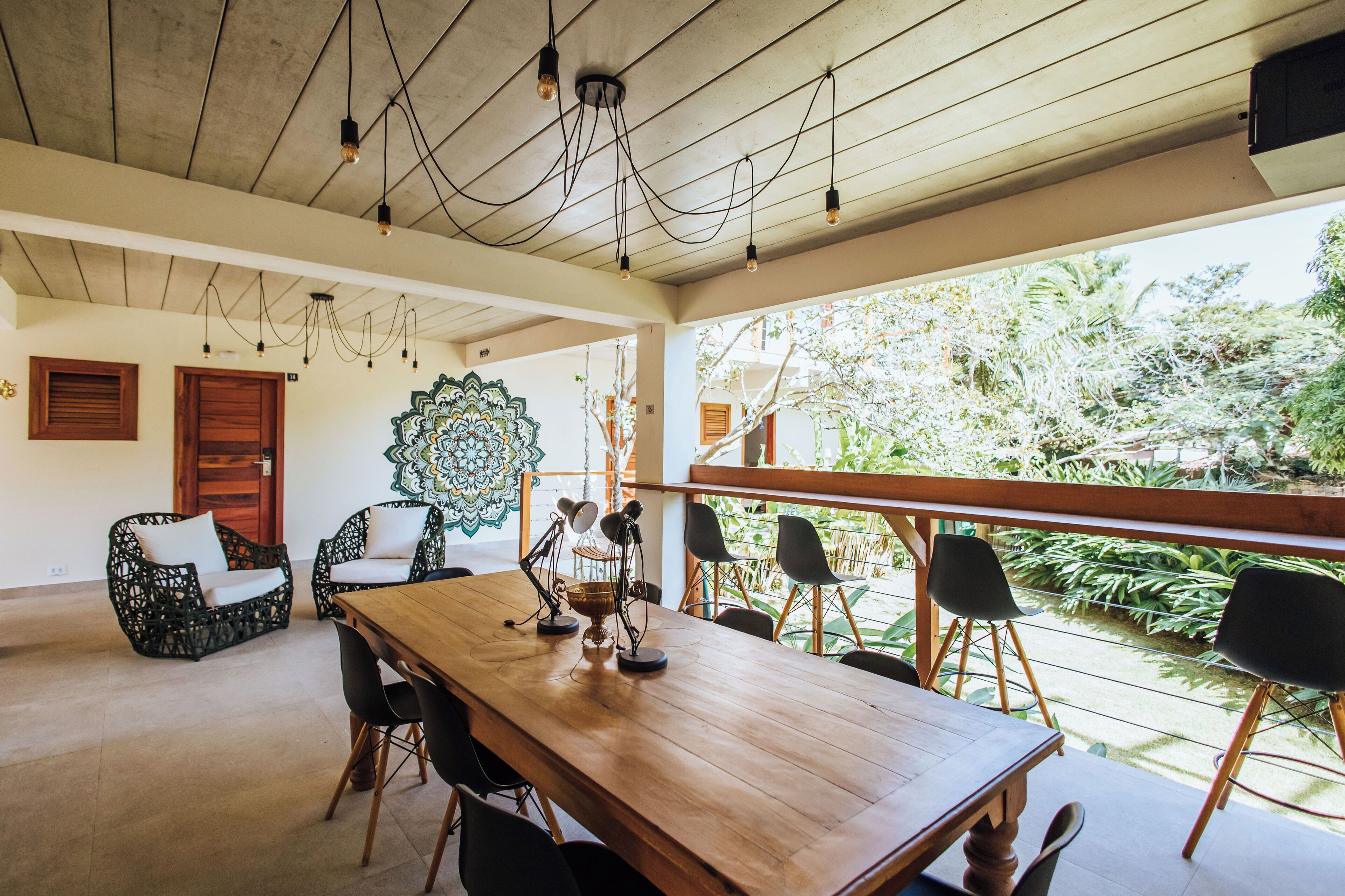 A spacious dining area with a wooden table and chairs, a decorative wall piece, and a view of greenery outside.