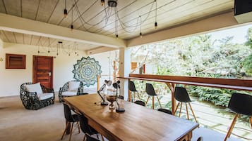 A spacious dining area with a wooden table and chairs, a decorative wall piece, and a view of greenery outside.